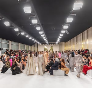 Multiple models on the runway at Dubai Fashion Week, wearing elegant outfits, with audience seated on both sides of the runway.