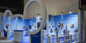 Messestand von Disney auf der ITB mit blauem Boden, weißer Standarchitektur und einer überdimensionalen Micky-Maus-Silhouette. Die Rückwand zeigt mehrere kreisförmige Disney-Illustrationen sowie ein zentrales Schlossmotiv, ergänzt durch Stehtische und Hocker.