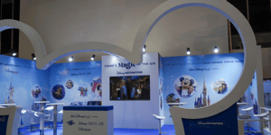 Ansicht des Disney-Messestands mit einer großformatigen weißen Micky-Maus-Kontur im Vordergrund. Der Stand umfasst eine Präsentationsfläche mit Bildschirm, mehrere Stehtische und blau gestaltete Wandflächen mit Disney-Grafiken und einem Schlossmotiv.
