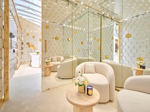 Pop-up-Laden mit geometrischem Wandmuster in Weiß und Gold, hell beleuchtet, mit Schmuckauslagen und modernen Sitzmöbeln.