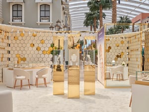 Luxuriöser Innenraum mit weiß-goldenem hexagonalem Wanddesign, eleganten weißen Stühlen und Tischen sowie Schmuckvitrinen.