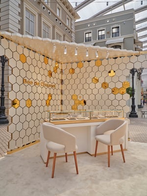 Eleganter Verkaufsraum mit gold-weißer Wandgestaltung, Glasvitrinen für Schmuck und stilvollen Sitzgelegenheiten.