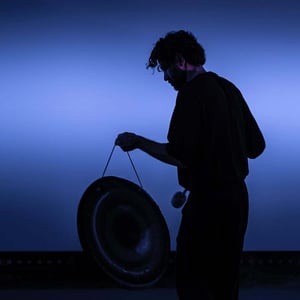 Person striking a gong against a blue background in an atmospheric light setting during the Dubai Future Foundation Event.