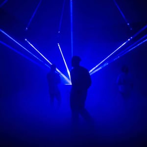 Silhouettes of people against a blue backdrop with laser beams and fog effects during the Dubai Future Foundation Event..