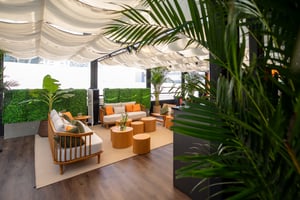 Outdoor‑Lounge des Breitling‑Pavillons mit modernen Sitzmöbeln, Begrünung und teilüberdachter Stoffbespannung.