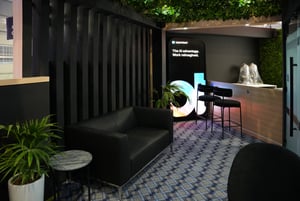 Lounge area of the OpenText booth with seating, plants, and modern design for networking and discussions.
