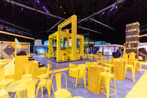 Indoor area with yellow chairs and tables and exhibition booths in the background