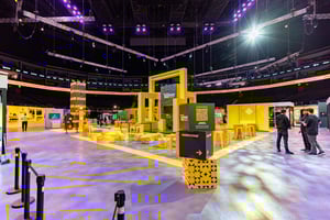 Innenbereich mit gelben Stühlen und Tischen sowie Messeständen im Hintergrund