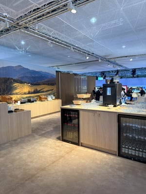 Catering and hospitality area of the Brückner Group booth with a counter, coffee machine, and backdrop of a mountain landscape.