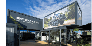 Außenansicht des Mercedes-Benz Defence Trucks Messestands mit großformatigem LED-Screen, Markenbotschaft und Containerarchitektur.