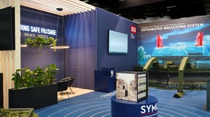 Messestand von GCS mit blauem Designkonzept, digitalem Display und ausgestellter Minenräumtechnik. Im Hintergrund zeigt eine großformatige Grafik das „Integrated Breaching System“, während ein begrünter Lounge-Bereich zum Verweilen einlädt.