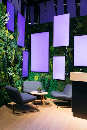 Detailansicht des Haufe Group Messestandes mit grüner Pflanzenwand und dekorativen, lilafarbenen Panels für ein modernes Ambiente.