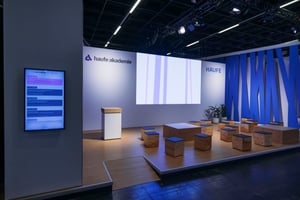 Messestand der Haufe Group auf der ZPE 2025 mit Bühne, Sitzwürfeln und großem Display für Präsentationen der Haufe Akademie.