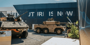 Militärische KNDS-Fahrzeuge auf dem Außengelände vor der dunklen Gebäudefassade mit dem beleuchteten Schriftzug „FUTURE IS NOW