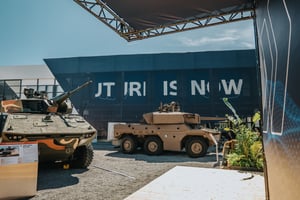 Militärische KNDS-Fahrzeuge auf dem Außengelände vor der dunklen Gebäudefassade mit dem beleuchteten Schriftzug „FUTURE IS NOW