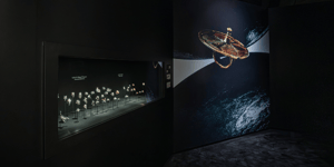 A jewelry display includes a case with small objects and a large photograph of a jewelry piece on the wall behind it.