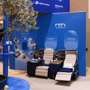 A close-up of the Lufthansa Group stand at ITB 2026, featuring aircraft seats for visitors to try out against a blue backdrop.