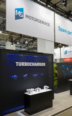 Product presentation at the MS Motorservice exhibition stand featuring an illuminated turbocharger display and branded graphics.