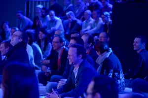 Teilnehmende sitzen in Reihen und verfolgen interessiert eine Präsentation oder Vorführung außerhalb des Bildausschnitts.