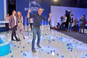 Eine interaktive Aktivität mit Teilnehmern, bei der eine Person sich zwischen verstreuten blauen und weißen Bällen auf dem Boden bewegt – ein spielerischer Programmpunkt.