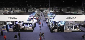 Wide view of Automate Show floor with NEURA Robotics booth prominently in the center, surrounded by other exhibitors and visitors.