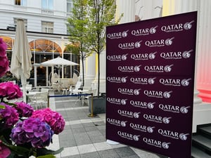 Ein dekorierter Außenbereich mit Blumenarrangements und einem Hintergrundbanner, auf dem mehrfach das Logo von Qatar Airways erscheint.