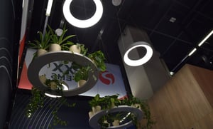 Detailansicht des Rexx Systems Messestandes mit von der Decke hängenden kreisförmigen Lampen und Regalen, die Pflanzen halten.