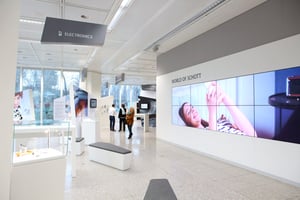 Ein moderner Raum mit mehreren Bildschirmen, auf denen verschiedene Inhalte gezeigt werden. Menschen bewegen sich durch den Raum.