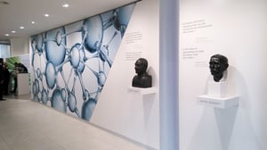 Ein Ausstellungsraum mit zwei Büsten und einer Wand mit einem wissenschaftlichen Muster. Die Büsten sind mit „OTTO SCHOTT“ und „ERNST ABBE“ beschriftet.