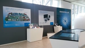 Ein weiterer Bereich des Ausstellungsraums zeigt verschiedene Exponate und ein großes Poster über eine Produktionsstätte. Ein weiteres Schild trägt die Aufschrift „INNOVATION LAB“.