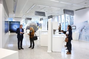 Zwei Personen stehen in einem modernen Ausstellungsraum und unterhalten sich. Im Hintergrund ist ein Schild mit der Aufschrift „INNOVATION LAB“ zu sehen.