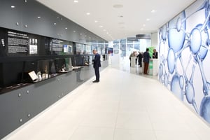 Moderner Showroom mit Informationstafeln über die Gründung eines Glaslabors im Jahr 1884, historischer Markengeschichte und wissenschaftlichen Grafiken, die Molekülstrukturen zeigen.