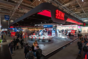 Eckansicht des SEW-EURODRIVE Messestandes auf der Hannover Messe 2026 mit schwarzem Dach, rotem Logo und einem großen runden Designelement mittig auf dem Stand.