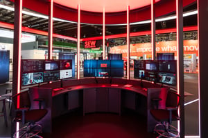 A close-up of the SEW stand at the 2026 Hannover Messe, featuring vertical LED tubes and a cockpit-style design.