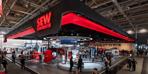 Eckansicht des SEW-EURODRIVE Messestandes auf der Hannover Messe 2026 mit schwarzem Dach, rotem Logo und einem großen runden Designelement mittig auf dem Stand.
