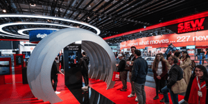 Großes rundes Exponat auf dem SEW Messestand mit Besuchern, die das Exponat begutachten.