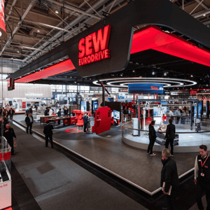 Exhibition stand featuring the C8 stand-building system for SEW-EURODRIVE at the Hannover Messe, in a black-and-red design, with visitors standing at the stand.