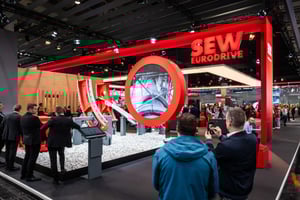 Messestand von SEW EURODRIVE auf der HANNOVER MESSE 2024 mit auffälligem roten Design und großem kreisförmigem Exponat im Vordergrund. Besucher erkunden die Präsentationsfläche.