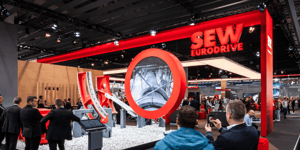 SEW-EURODRIVE booth at HANNOVER MESSE 2024 featuring a striking red design and a large circular exhibit in the foreground. Visitors are exploring the display area.