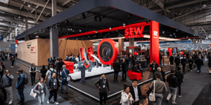 Overall view of the SEW-EURODRIVE booth with striking red design, circular exhibit, and numerous attendees learning about drive technology and automation solutions.
