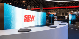 Large LED display with SEW-EURODRIVE logo at the booth, surrounded by interactive presentation zones for innovative drive technology.