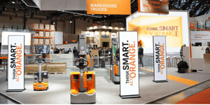 Front view of the STILL booth displaying warehouse trucks and prominent signage with the message ‘Think Smart. Act Orange’.