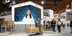 STILL booth at LogiMAT 2025 featuring a large LED screen and displayed warehouse technology solutions. Products such as spare parts and industrial trucks are visible in the foreground.
