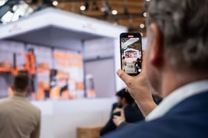 Nahaufnahme eines Besuchers, der den STILL-Messestand fotografiert. Im Hintergrund ist ein großes Display mit Regalsystemen und Lagertechnik zu sehen.