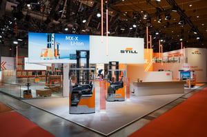 A corner view of the STILL exhibition stand at LogiMAT 2026, featuring forklift trucks, large LED screens and orange elements in line with the corporate identity.