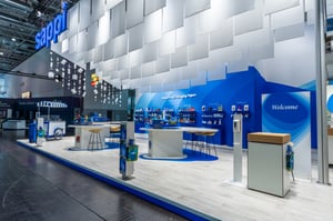 Gesamtansicht des Messestands von Sappi mit einem Willkommensschild, von der Decke hängenden Papierrollen und mehreren Schreibtischen.
