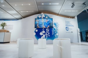 Infostand am Messestand von Sappi mit Sitzgelegenheiten aus Papier, Papierdekorationen und einem Bildschirm mit informativen Inhalten.