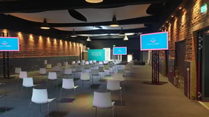 Leerer Konferenzraum mit Reihen von Stühlen und einer Bühne mit großem Bildschirm.