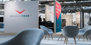 Moderner Messestand mit BAUKULTTOUR 21 Logo und Sitzgelegenheiten.