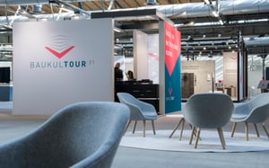 Moderner Messestand mit BAUKULTTOUR 21 Logo und Sitzgelegenheiten.